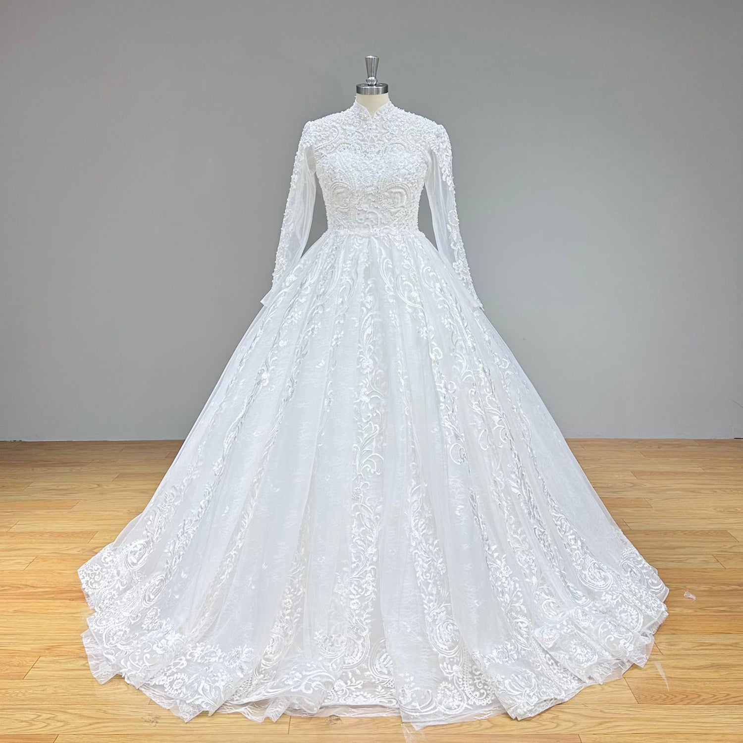 Classic full front studio view of a luxury high neck ball gown wedding dress on a mannequin, highlighting the perfectly fitted beaded pearl bodice, sheer sleeves, and voluminous glittering skirt.