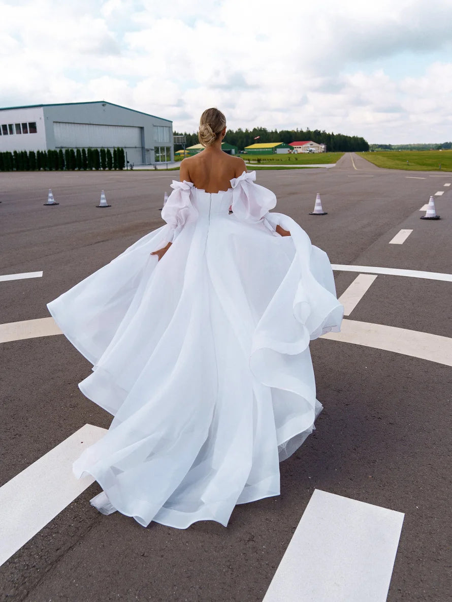 Back view of a stunning A-line wedding dress with a sweeping train, showcasing the elegant pleated bodice and detachable puff sleeves.
