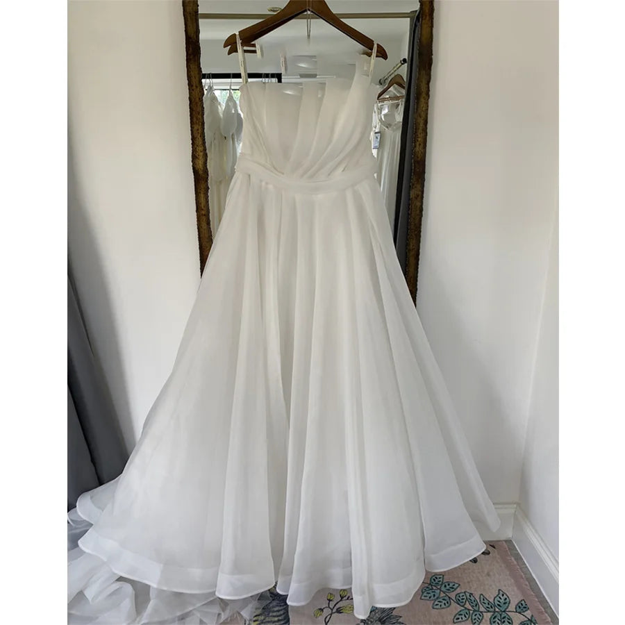 A simple yet sophisticated A-line bridal gown hanging on a rack, featuring a clean boat neck design and pleated skirt.