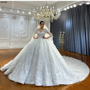 Full-length front view of a luxury long-sleeve ball gown wedding dress featuring a shimmering beaded bodice, high illusion neckline, and a grand cathedral train in a boutique showroom.