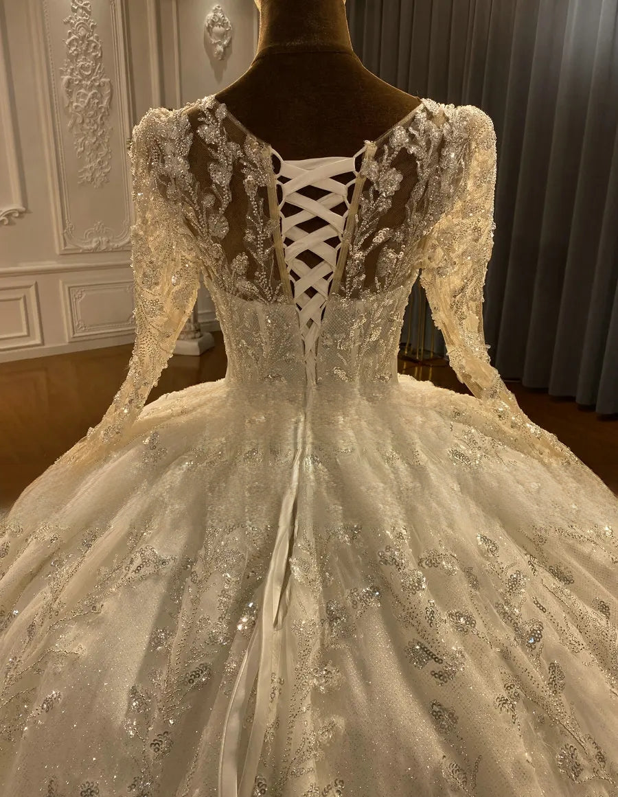 Detailed close-up of the back of an elegant long-sleeve bridal gown showcasing a traditional white lace-up corset closure and intricate silver leaf-motif embroidery.