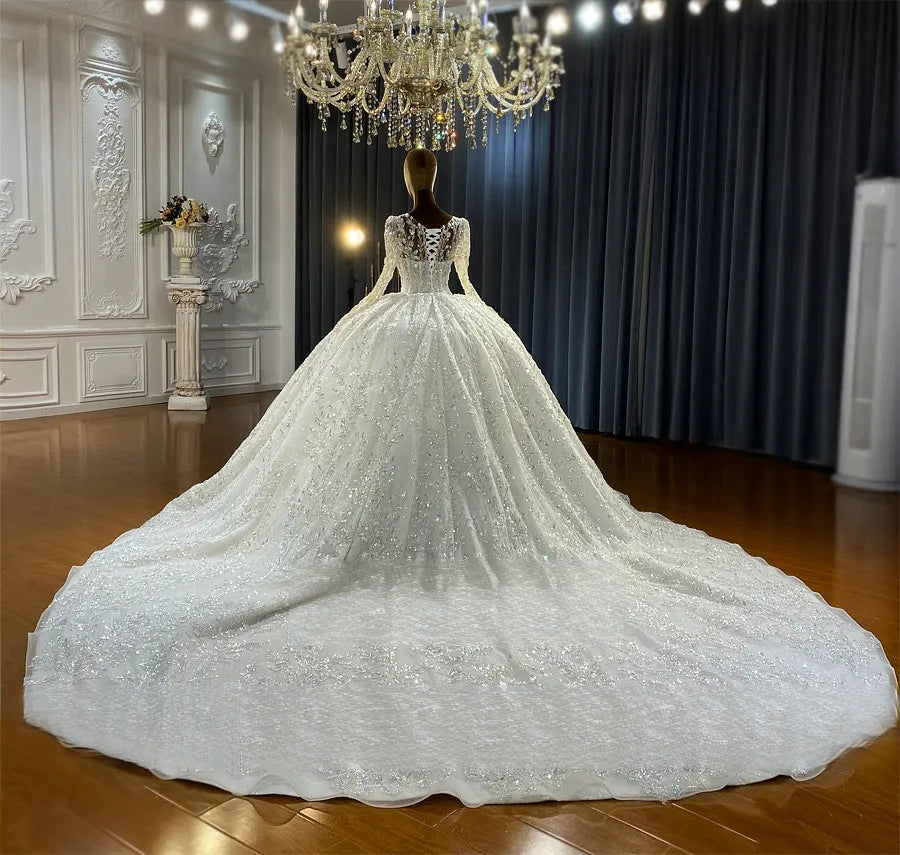 Professional showroom display of a luxury white ball gown bridal dress showing the intricate corset back detailing and the expansive flow of a shimmering, embroidered long train.