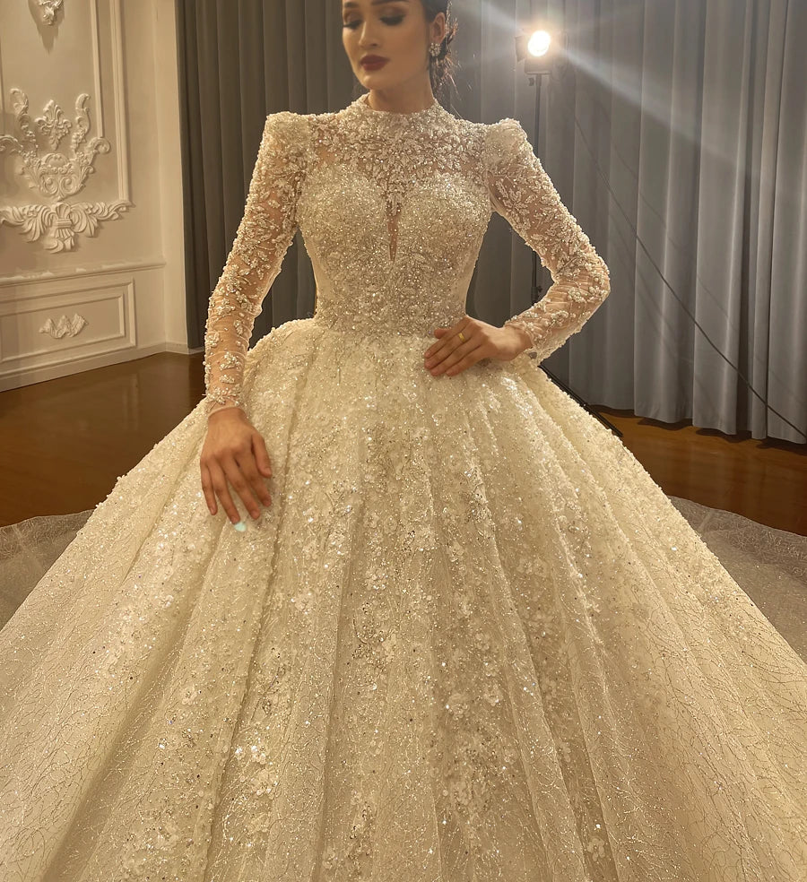 Close-up detail of the bodice on a luxury long sleeve wedding dress, highlighting the elegant hand-beaded lace appliques and sheer high-neck design.