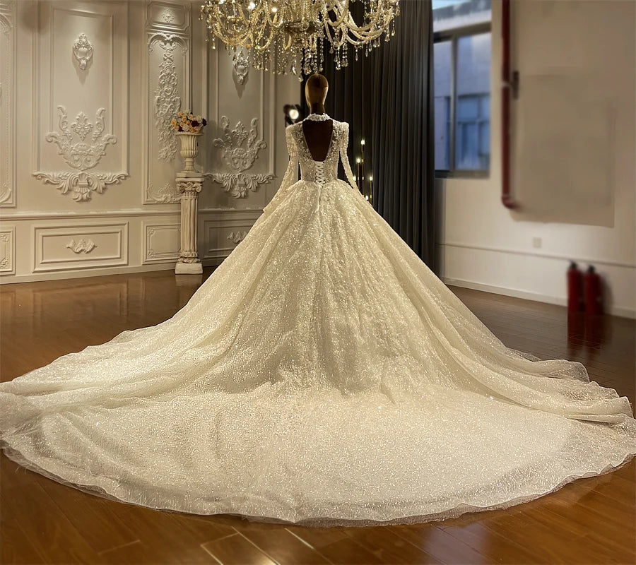 Detailed back view of a luxury long sleeve bridal gown, emphasizing the classic lace-up corset closure, sheer illusion back detailing, and magnificent long train.