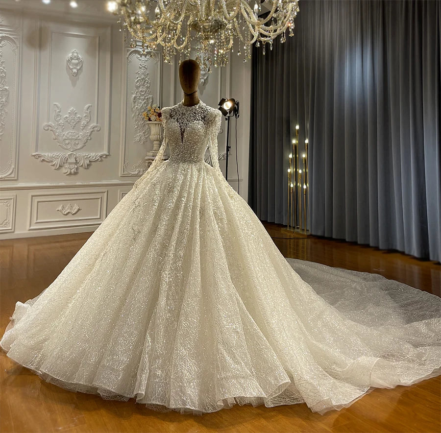 Professional showroom display of a luxury sparkly ball gown wedding dress on a mannequin, illustrating the elegant long sleeves and the grand scale of the sequined skirt.