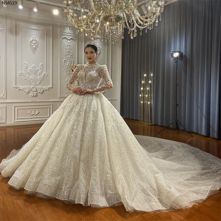 Front perspective of an elegant model wearing a new design luxury long sleeve ball gown wedding dress, paired with a classic bridal tiara in a sophisticated setting.