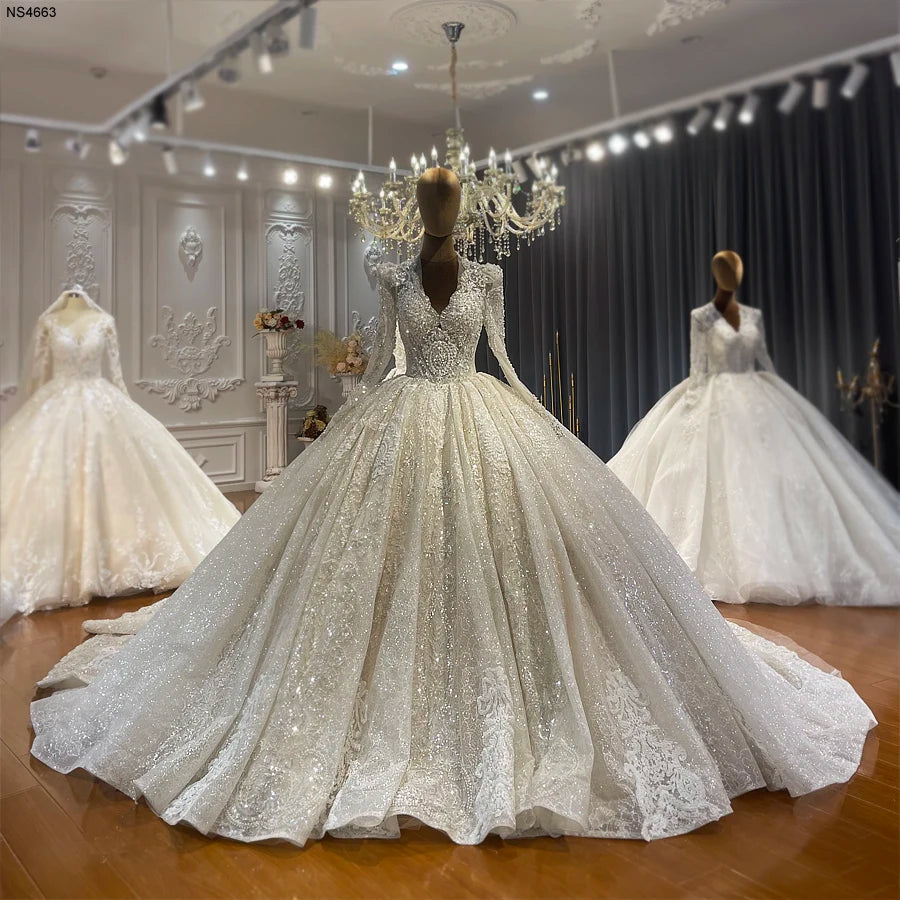 Detailed display of a hand-beaded lace ball gown wedding dress with a deep V-neckline and long sleeves on a mannequin, highlighting the premium fabric and heavy embroidery.