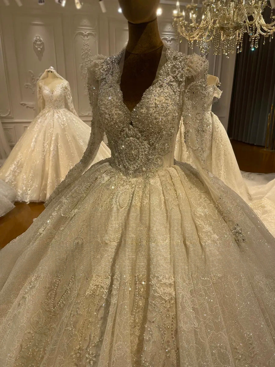 Close-up detail of a luxury hand-beaded lace bridal dress featuring a plunging V-neckline, sheer long sleeves, and intricate shimmering embroidery on a mannequin.