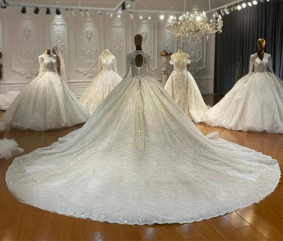 Rear view of a magnificent lace ball gown wedding dress on a mannequin, showcasing the keyhole back, lace-up corset, and an expansive sparkling circular train in a bridal boutique.