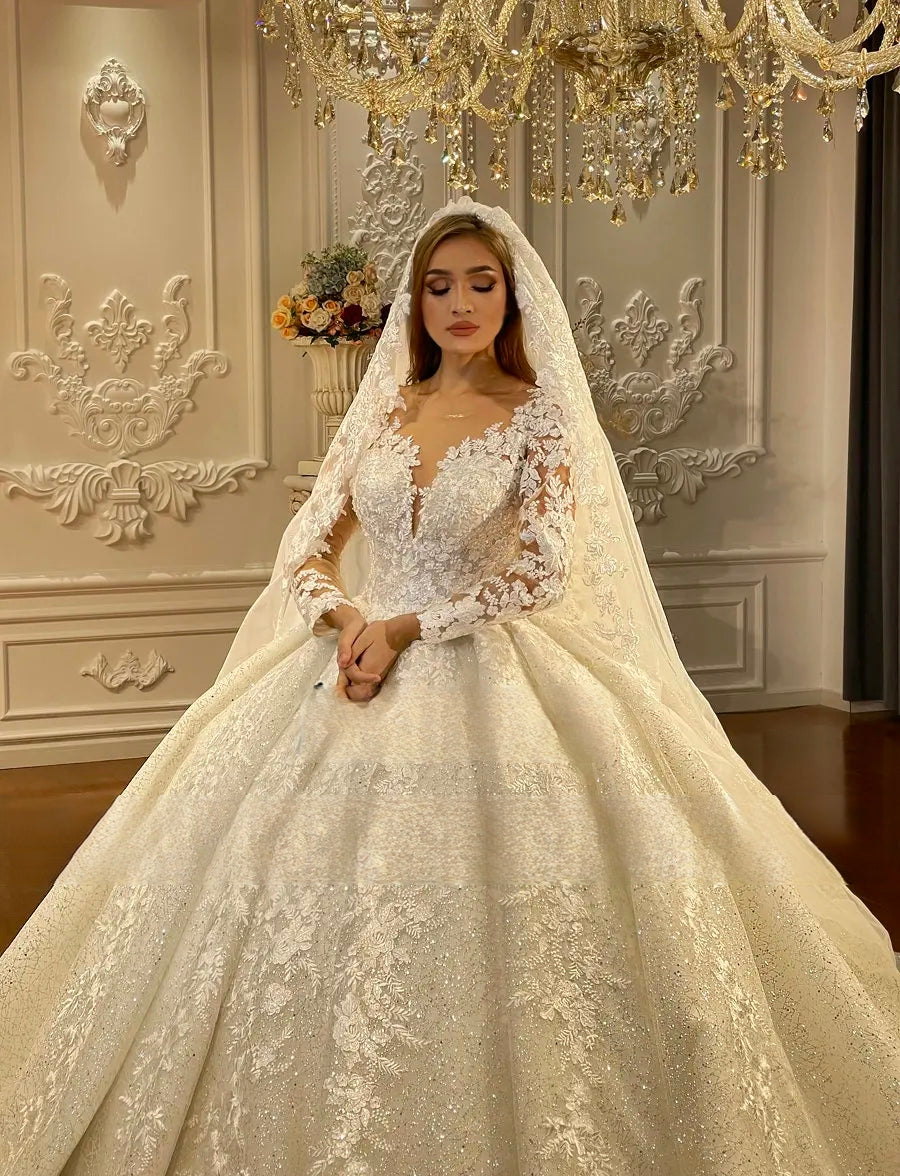 Close-up detail of the bridal gown's luxury bodice, showcasing high-quality hand-sewn lace appliques and shimmering beadwork on the illusion neckline and long sleeves, paired with a matching lace-trimmed veil.