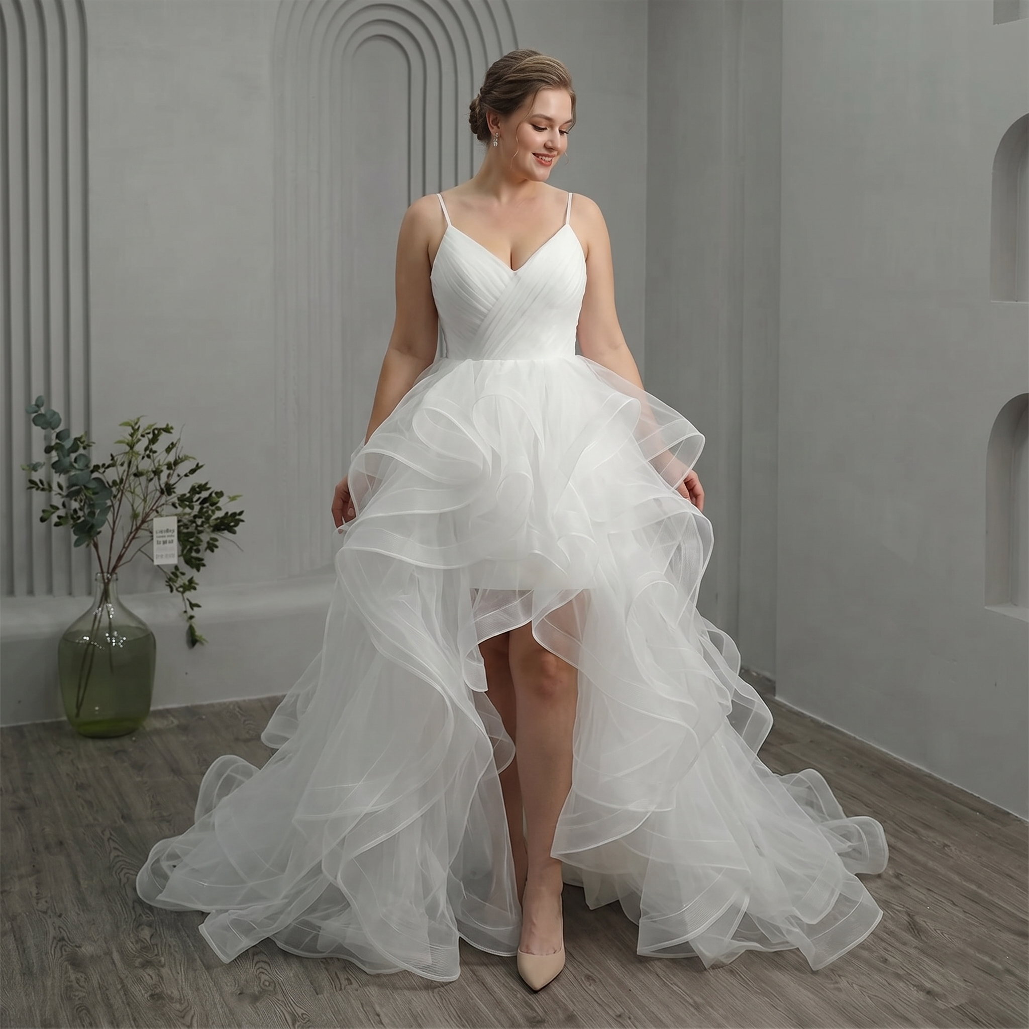 A model posing in a high-low bridal gown featuring voluminous tulle ruffles and a flattering V-neck bodice.