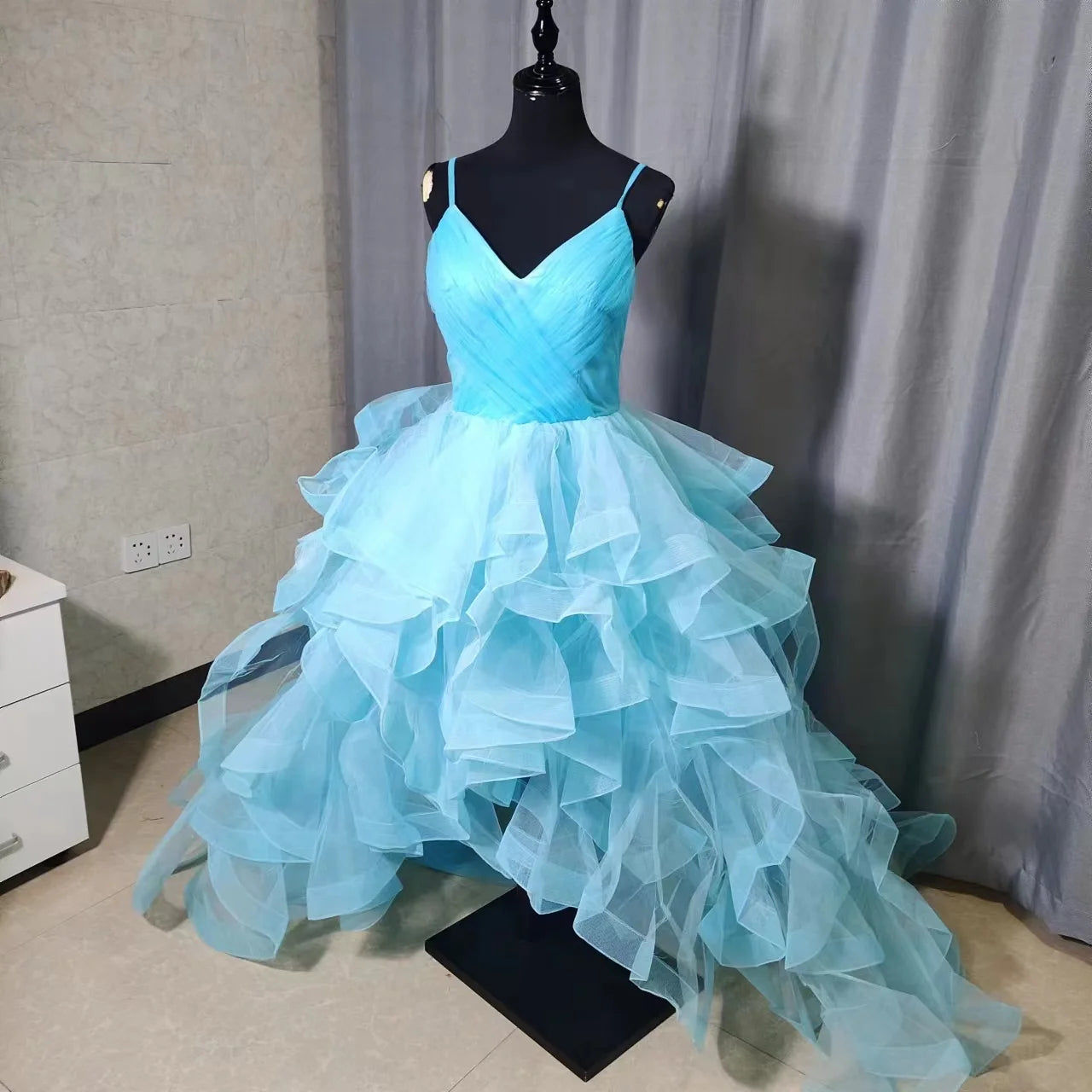A short front, long back high-low bridal gown in vibrant blue, featuring a V-neckline, spaghetti straps, and voluminous tiered tulle ruffles.