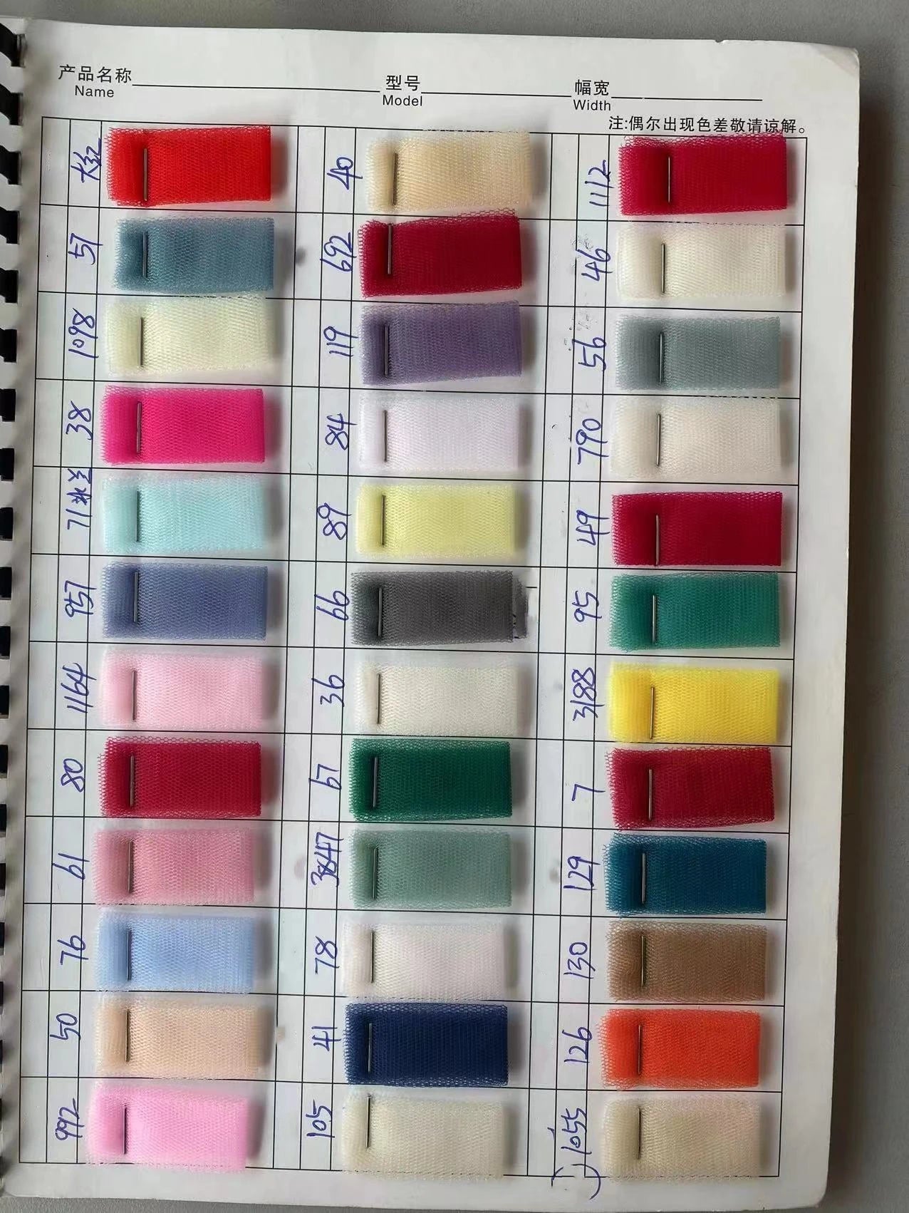 A comprehensive fabric color swatch book showing various tulle options for custom high-low bridal gowns, including reds, blues, and neutral tones.