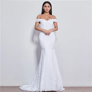 A beautiful bride posing in a white off-shoulder mermaid wedding dress with intricate lace detailing, holding a large floral bouquet.