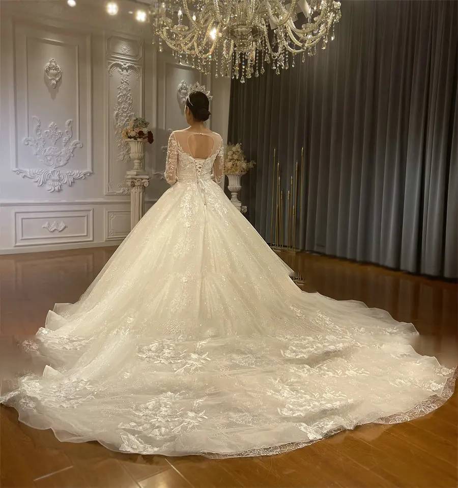 Back angle of a shimmering custom bridal gown emphasizing the expansive lace-trimmed train and traditional corset-style back.