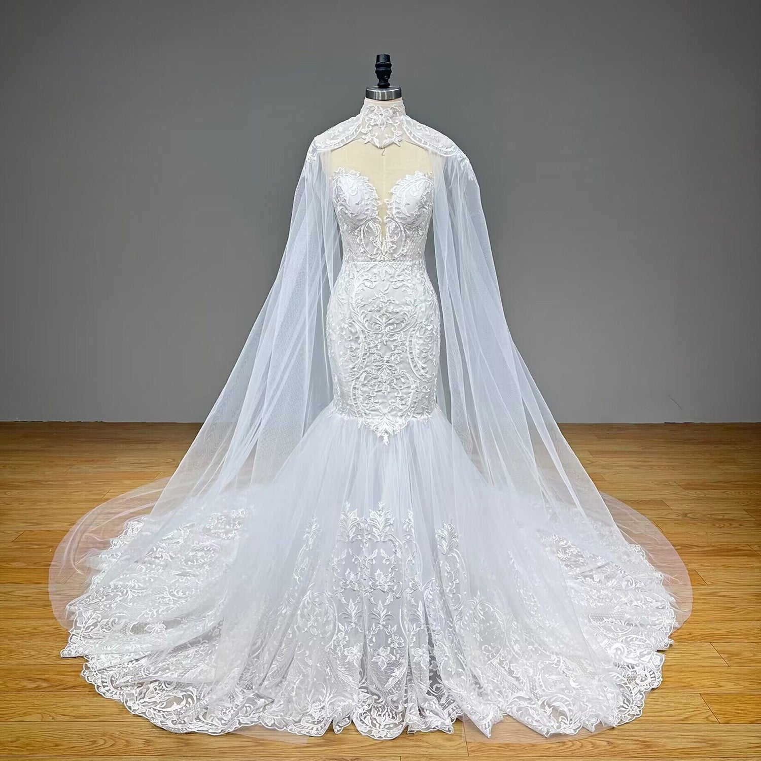 Full-length front view of a luxury tulle mermaid wedding gown with a matching high-neck sheer capelet, featuring an illusion plunging sweetheart bodice and a dramatic flared skirt.
