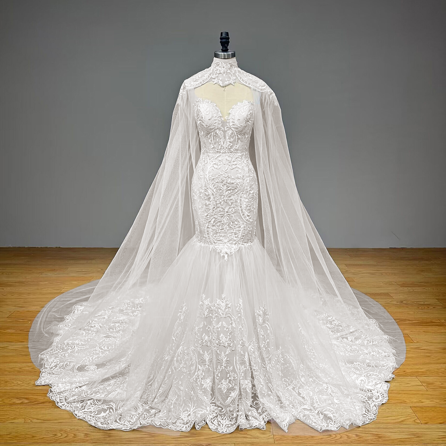 Direct studio product display of a convertible lace-appliqued mermaid wedding dress with its sweeping high-neck tulle shawl fully extended on a mannequin.