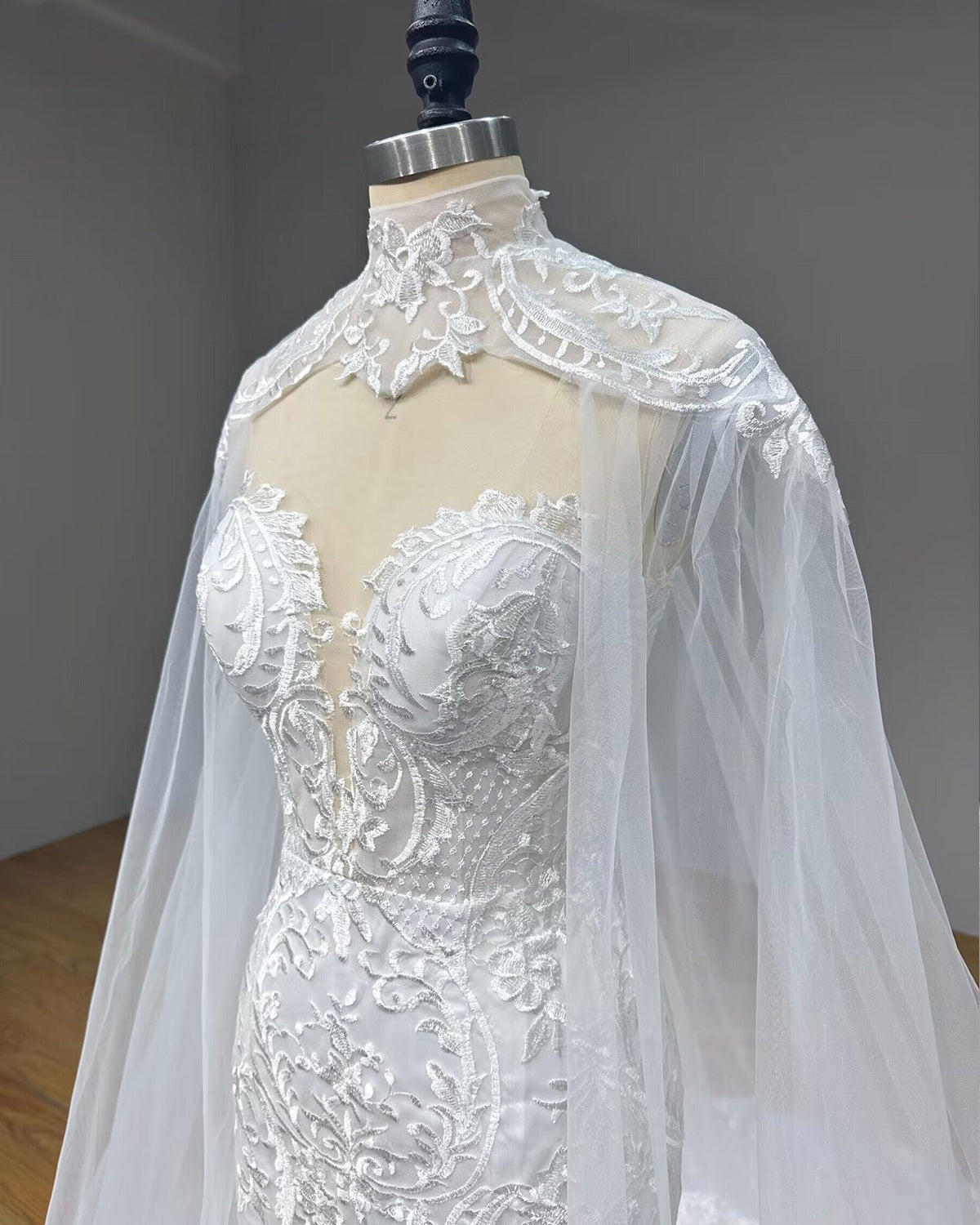 Angled close-up of a bridal bodice on a mannequin, emphasizing the sheer mesh plunging sweetheart neckline, structured corset design, and embroidered lace high-neck collar.