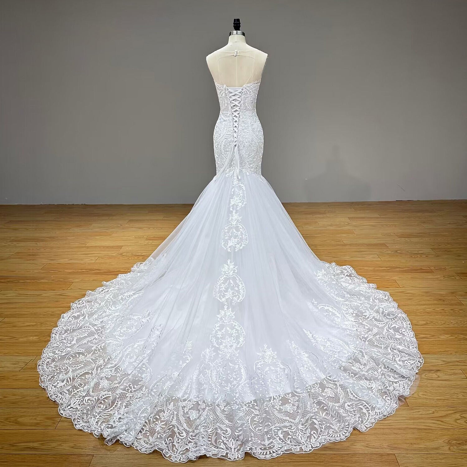 Full back view of the tulle mermaid wedding dress on a mannequin, highlighting the adjustable lace-up corset back closure and a long, scalloped lace cathedral train.