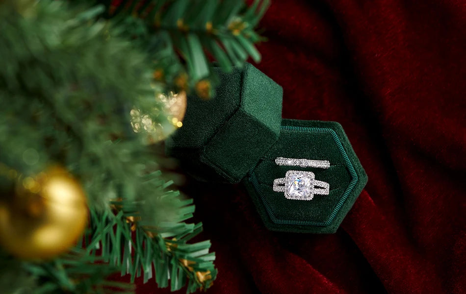 High-angle shot of the women's silver wedding rings nestled inside a green velvet hexagonal box next to Christmas tree branches.