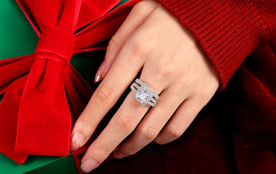 Model's hand wearing the 4ct princess-cut engagement ring and matching wedding band set, styled next to a festive red holiday bow.