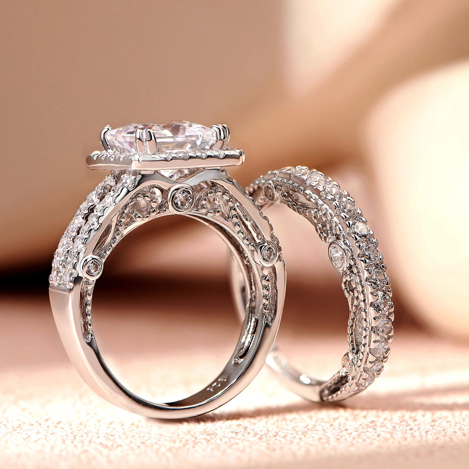 Macro view of a 925 sterling silver 4ct princess cut cubic zircon engagement ring displaying complex vintage openwork filigree detailing next to a matching wedding band.