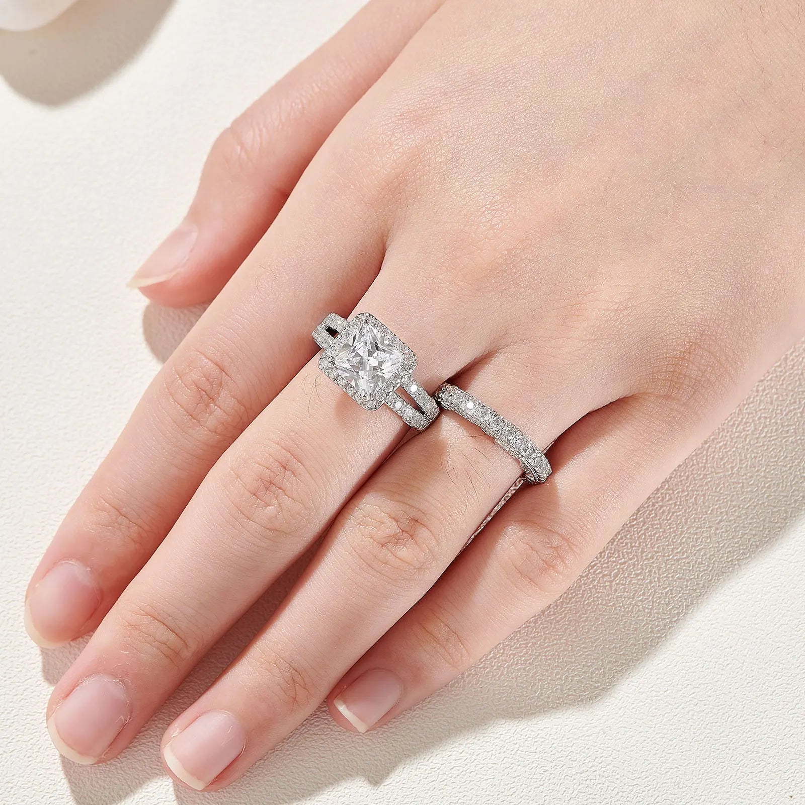 High-angle shot of a woman's hand showcasing the 2pcs princess cut cubic zircon bridal ring set on her finger under bright, clean lighting.