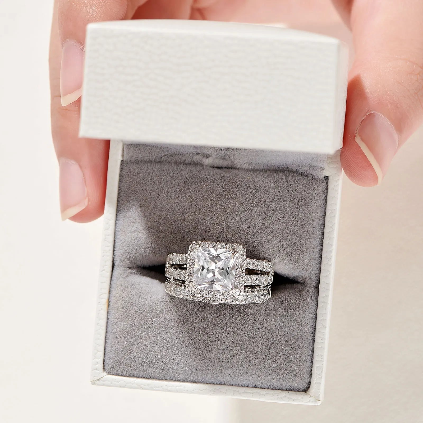 Front perspective of a vintage style sterling silver square halo princess cut wedding ring set safely nestled within a textured white jewelry gift box.