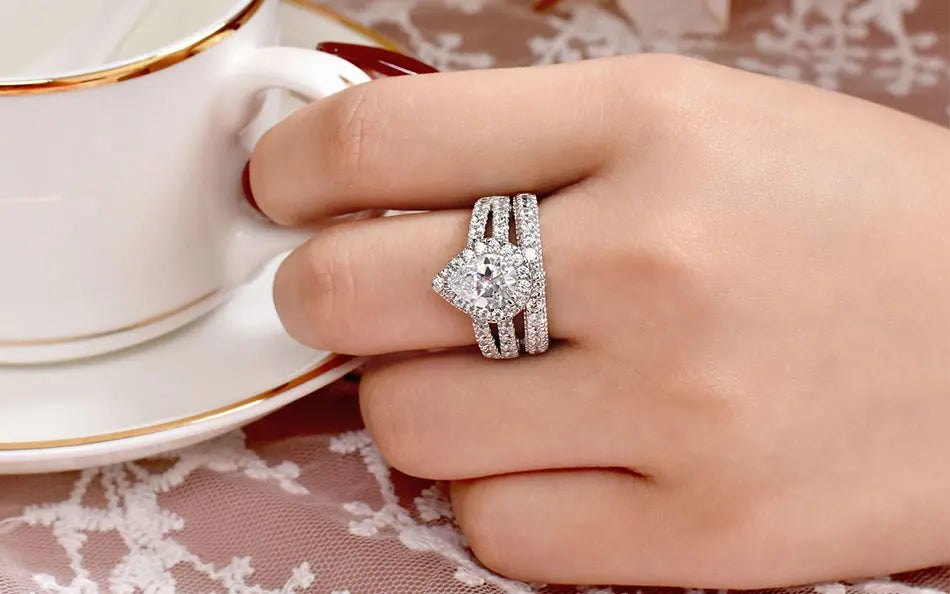 Close-up of a glamorous pear-shaped teardrop cubic zircon wedding ring set worn on a hand holding a white porcelain teacup.