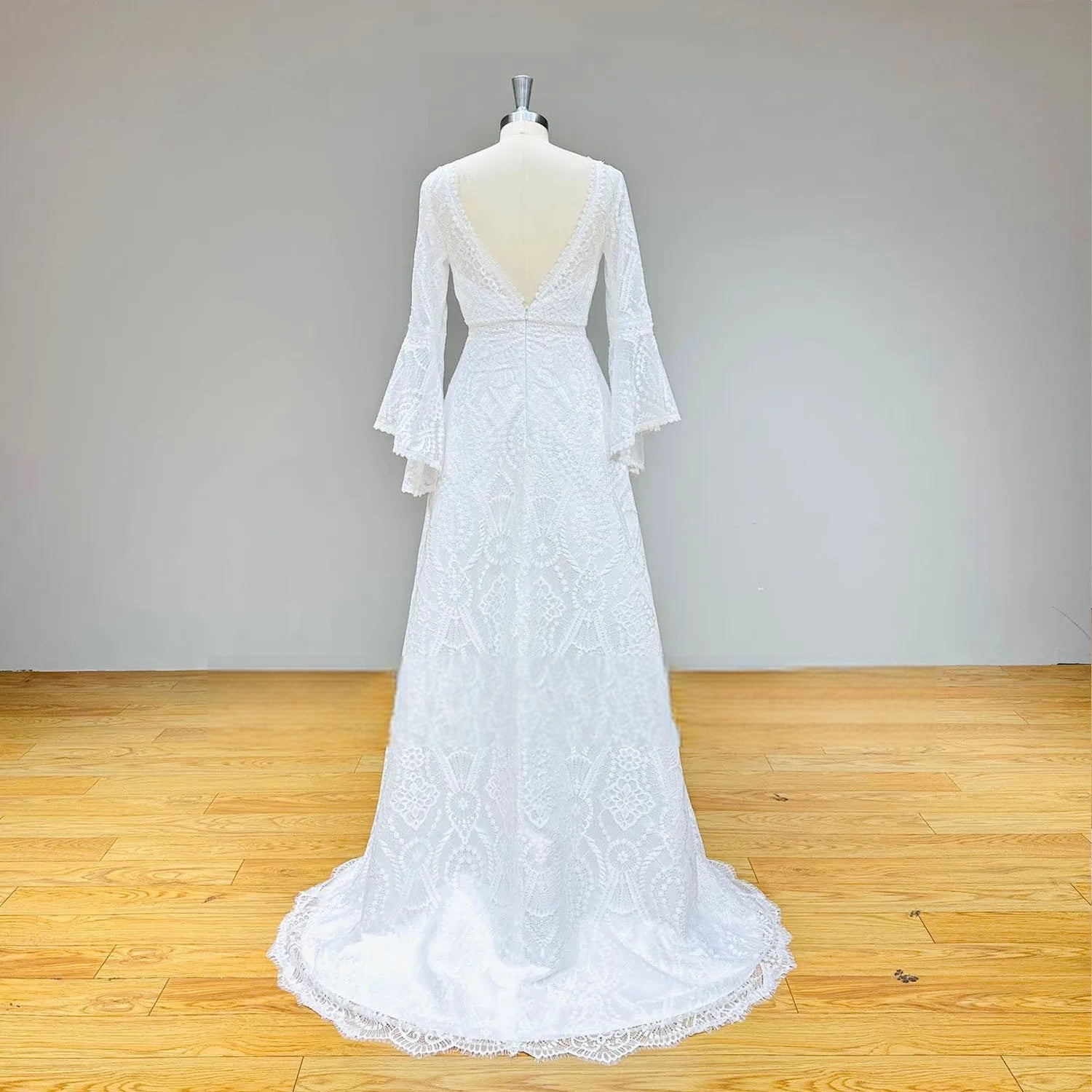 Rear view of the backless lace wedding gown on a mannequin, showcasing the deep V-back design and a sweeping lace-trimmed train.