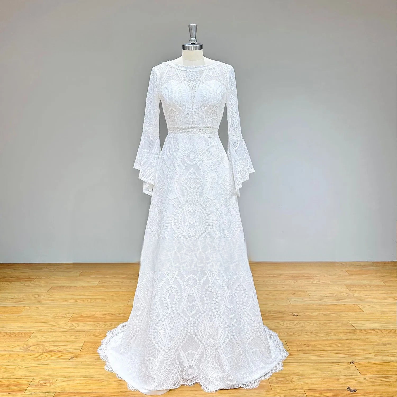 Studio front view of a long-sleeve geometric lace wedding dress on a mannequin, emphasizing the modest neckline and bohemian A-line silhouette.