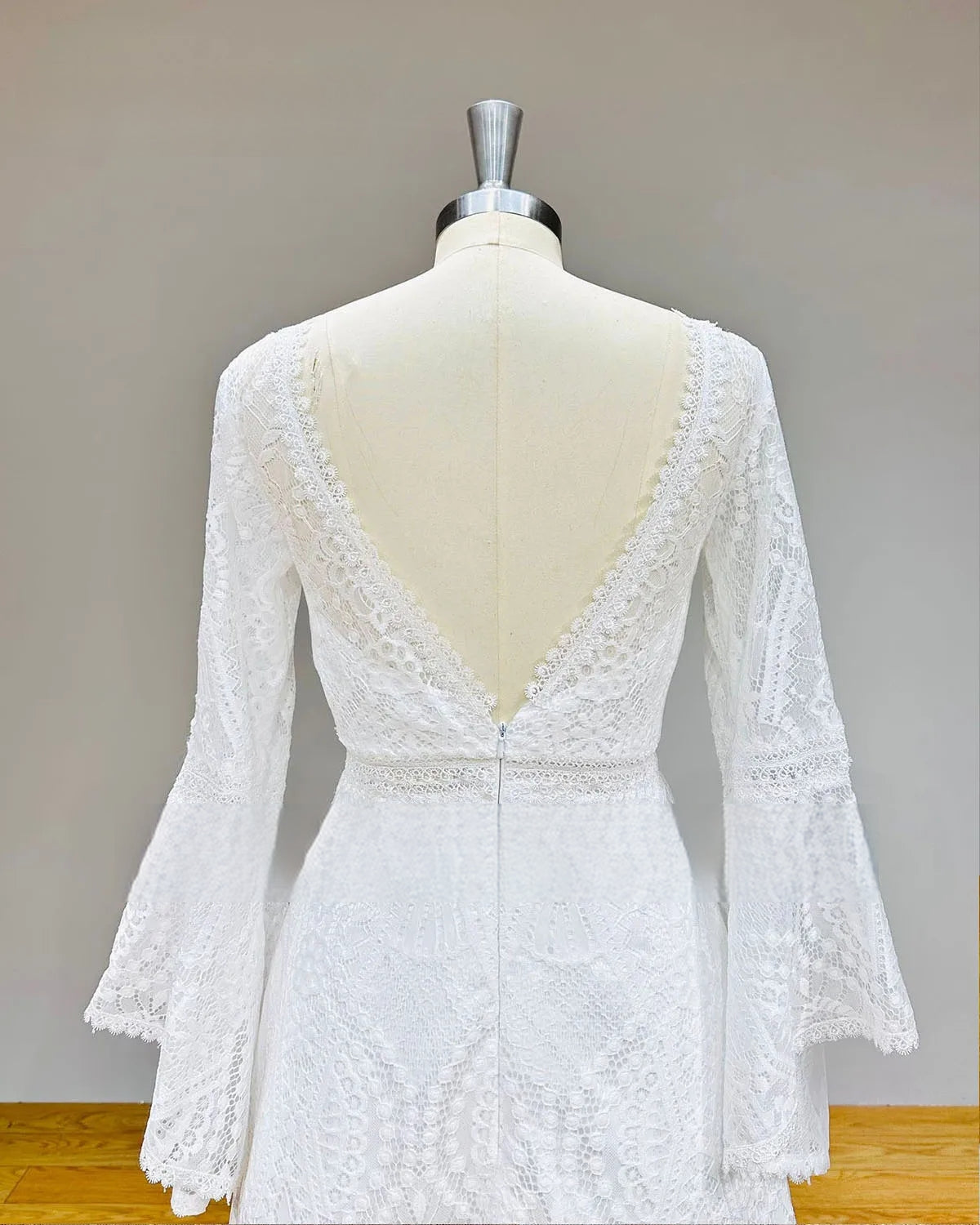 Close-up of the backless V-neckline of a lace bridal gown, featuring scalloped lace edges and sheer illusion long sleeves.