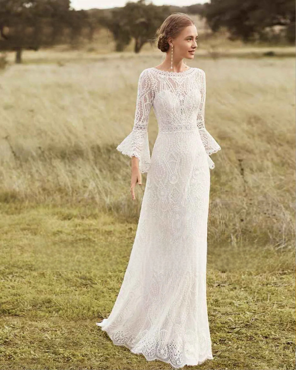 A romantic bride modeling an O-neck long-sleeve lace wedding dress with flared bell sleeves in a bohemian outdoor field setting.
