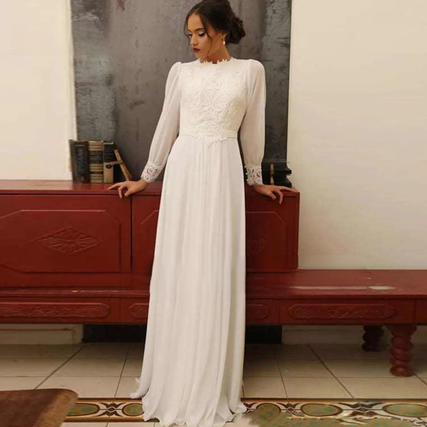 Brunette bride modeling a vintage-inspired long sleeve chiffon bridal gown, highlighting the modest high neckline and romantic pleated chiffon skirt.