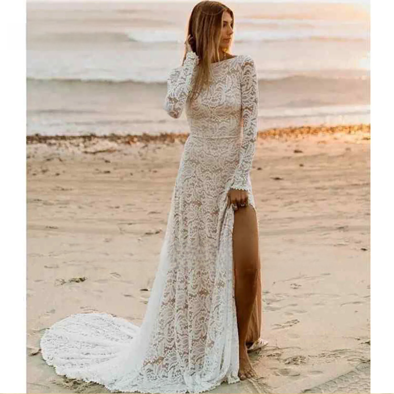 A bride standing on a sunset beach wearing a long sleeve lace wedding dress with a high skirt slit and a modest O-neckline, perfect for a destination wedding.