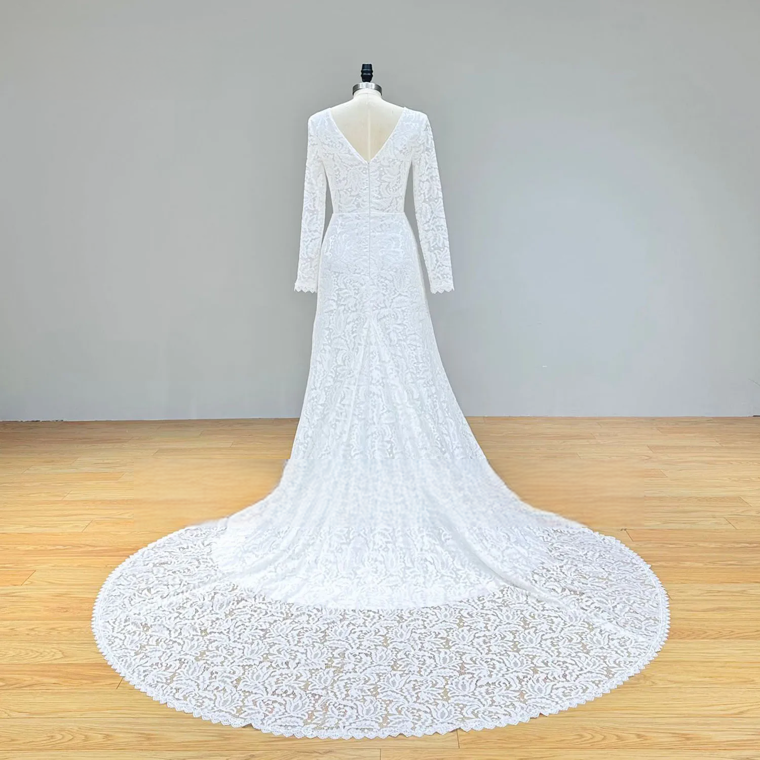 Rear view of a lace beach wedding dress on a mannequin, featuring a deep V-back with a discrete zipper-up closure and an expansive, decorative lace train.