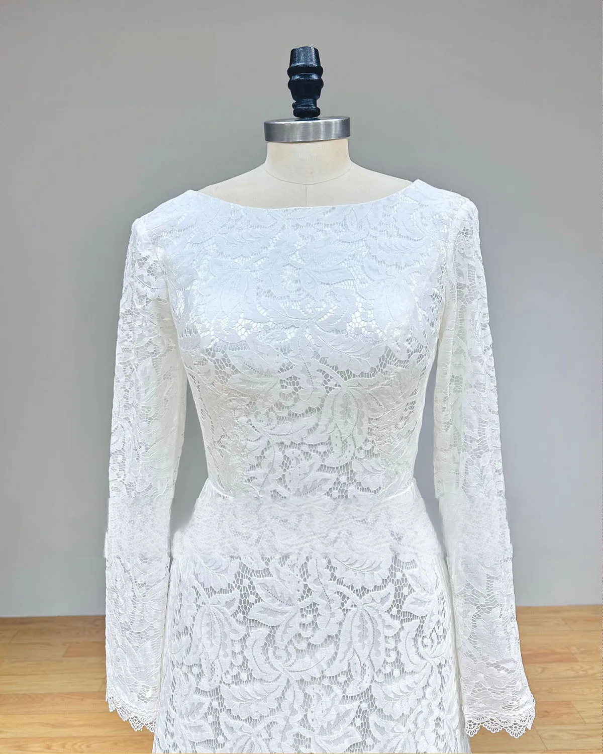 Close-up of the bodice on a white long sleeve lace wedding dress, highlighting the high O-neck and delicate floral embroidery.