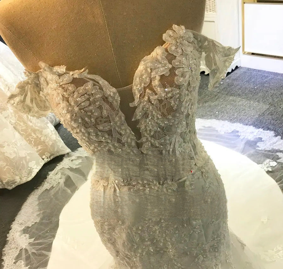 Detailed view of the intricate floral lace embroidery and sheer plunging illusion neckline on an off-shoulder beach wedding dress.