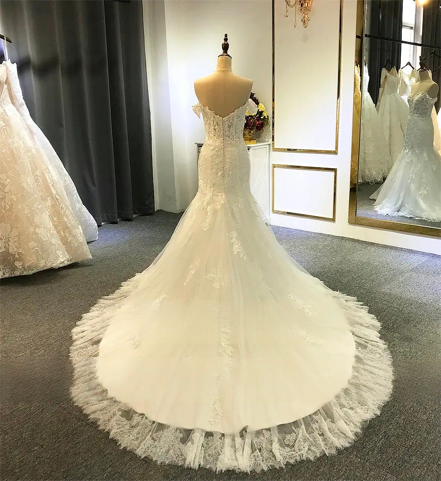 Rear view of the off-shoulder mermaid bridal gown on a mannequin, displaying a row of covered buttons down the back and a sweeping circular lace train.