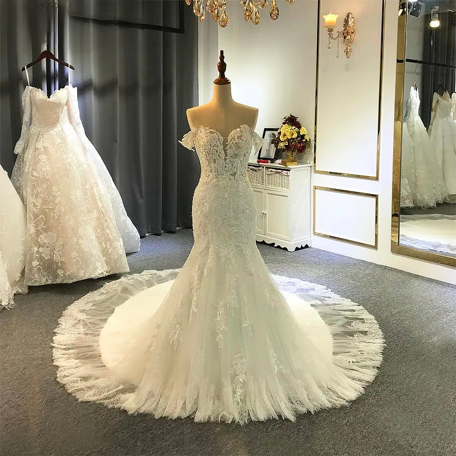 Another front view of the elegant off-shoulder beach bridal gown on a mannequin, highlighting its delicate lace design in a bridal boutique setting.