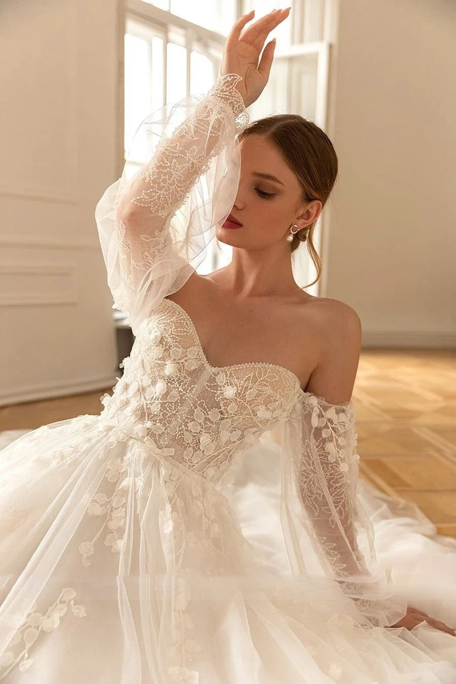Close-up of an elegant wedding gown showcasing long sheer sleeves, delicate lace floral embroidery, and a romantic sweetheart neckline.