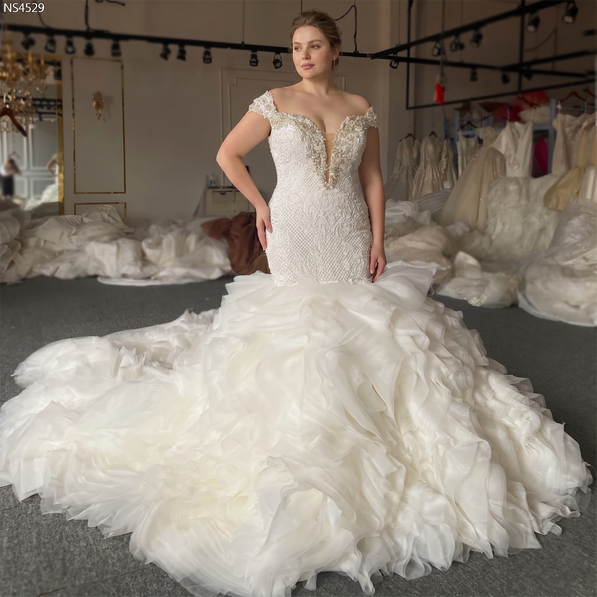 Stunning plus-size bride in a luxury beaded off-shoulder wedding gown with an intricate crystal-embellished bodice and voluminous detachable ruffle train.