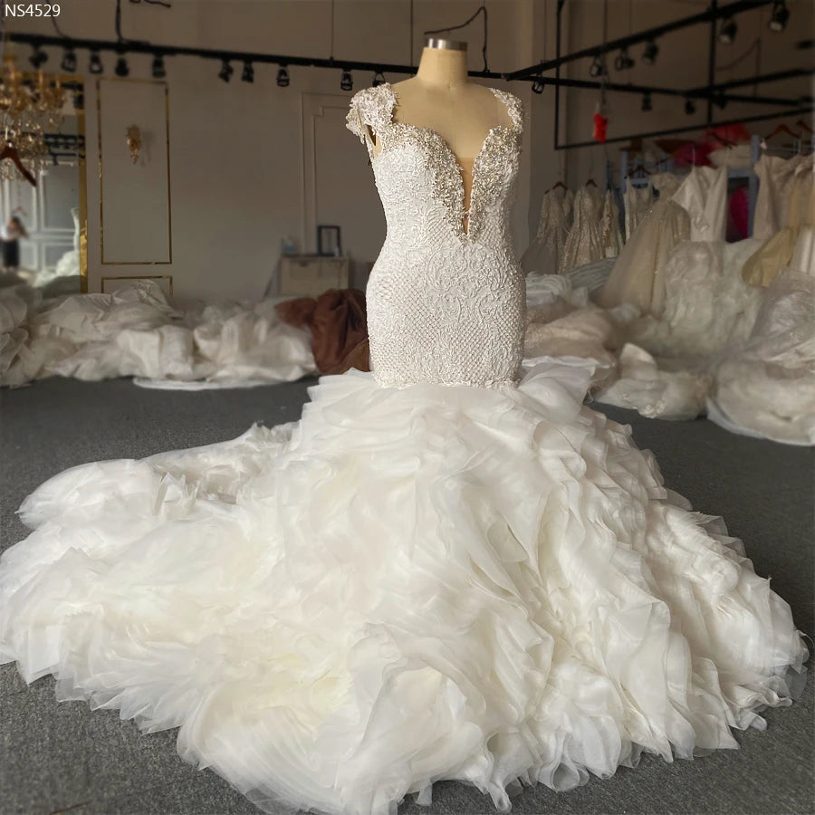 Elegant display of a 2-in-1 lace mermaid bridal gown on a mannequin, highlighting the contrast between the fitted beaded bodice and the grand removable ruffle skirt.