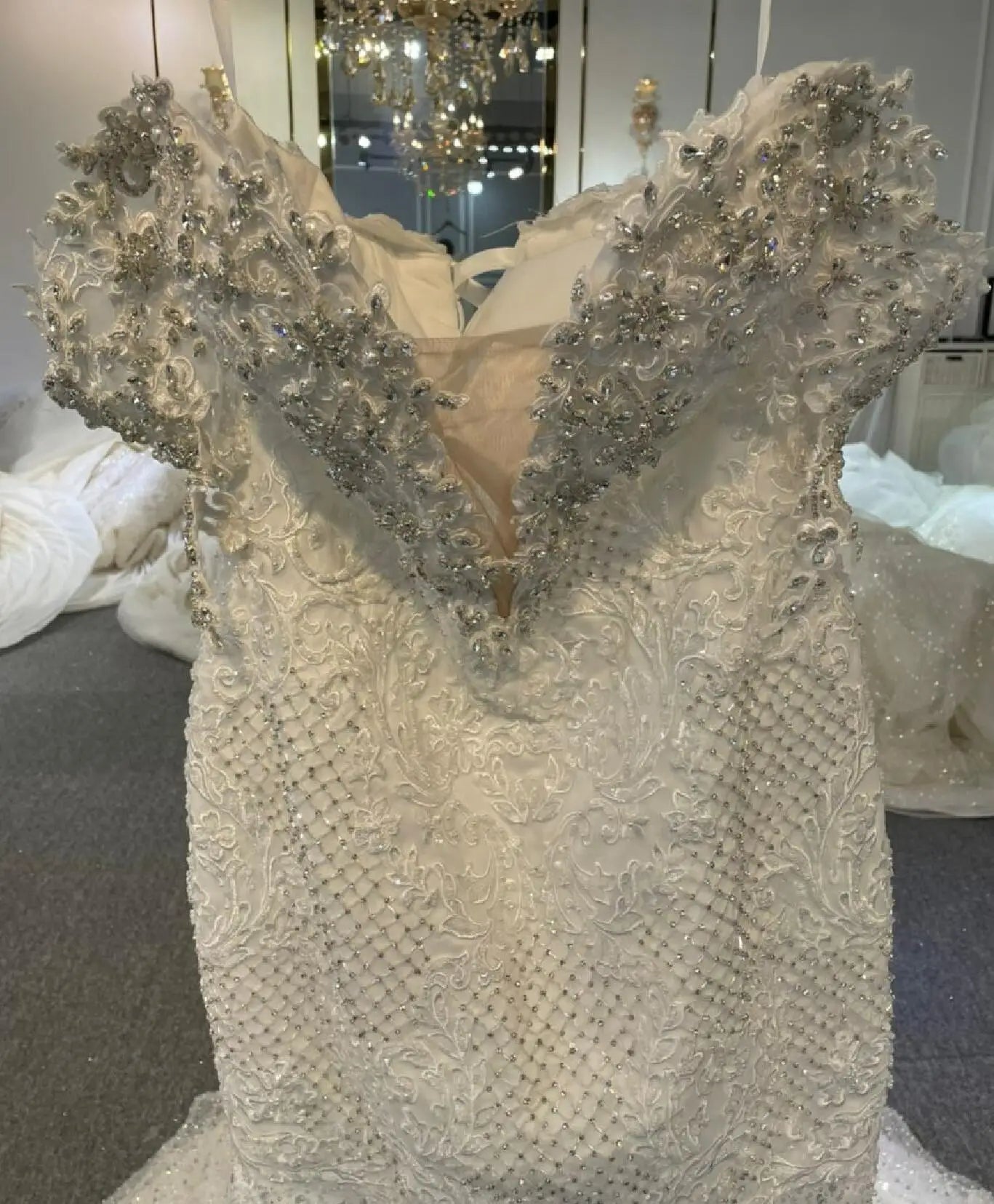 Close-up detail of the bridal bodice featuring exquisite hand-sewn crystal beadwork, intricate floral lace appliqués, and a sheer plunging V-neckline.