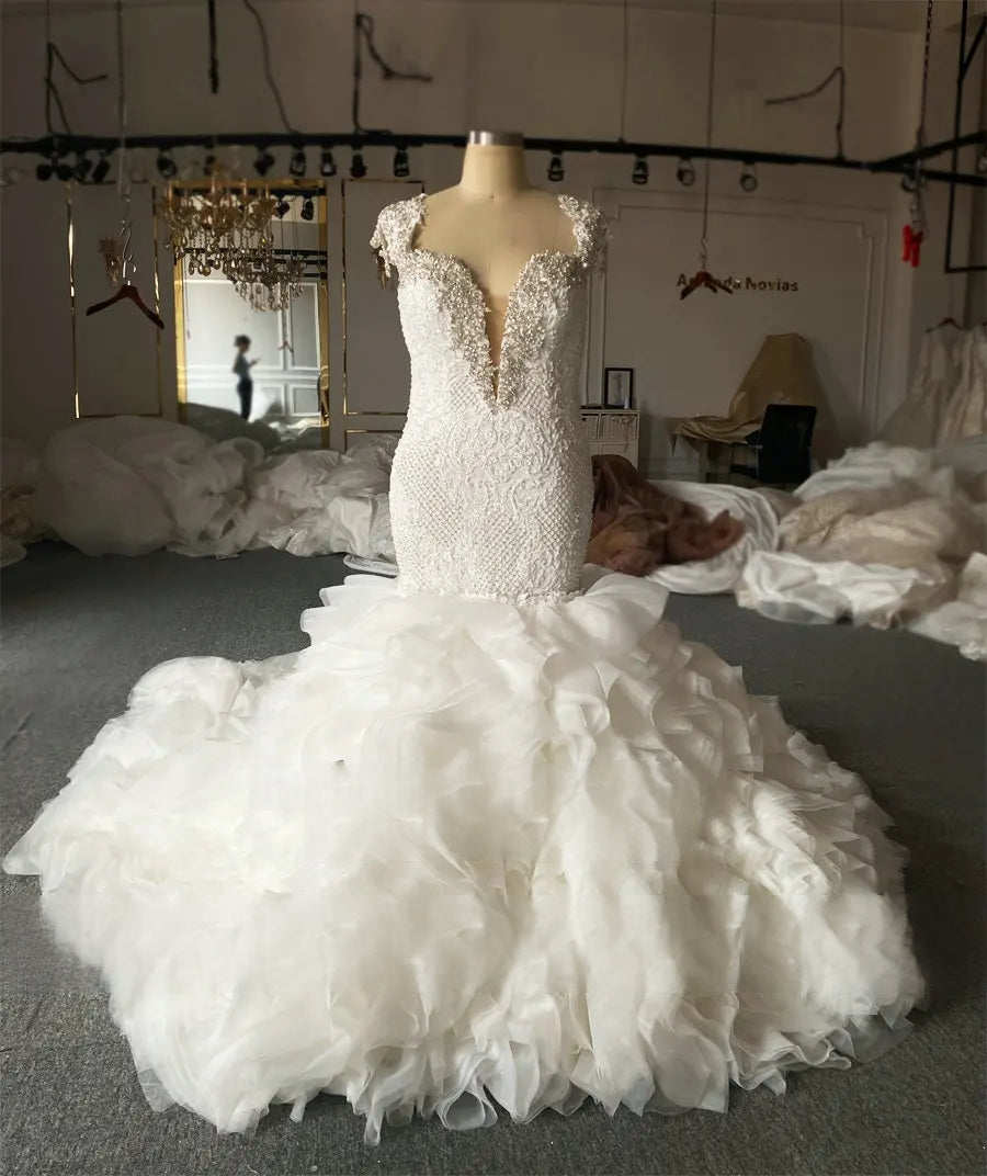 High-fashion showroom display of an off-shoulder beaded mermaid bridal gown with a majestic removable tiered ruffle overlay for a versatile bridal look.