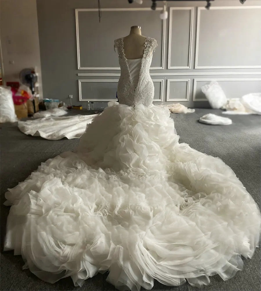 Breathtaking back view of the 2-in-1 bridal gown on a mannequin, emphasizing the expansive, tiered ruffle cathedral-length train and delicate off-shoulder lace sleeves.