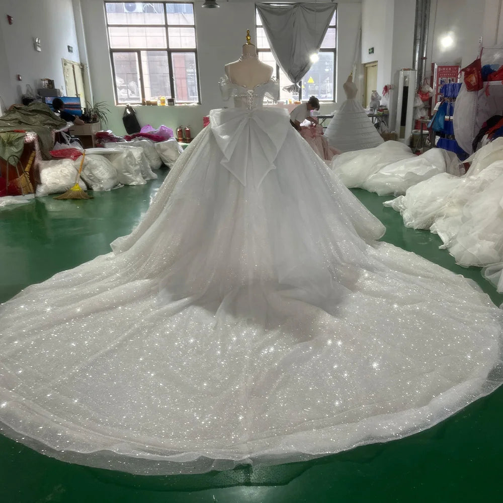 Breathtaking rear view of an off-shoulder princess wedding dress on a mannequin, showcasing a classic lace-up corset back and an expansive sparkling cathedral train.