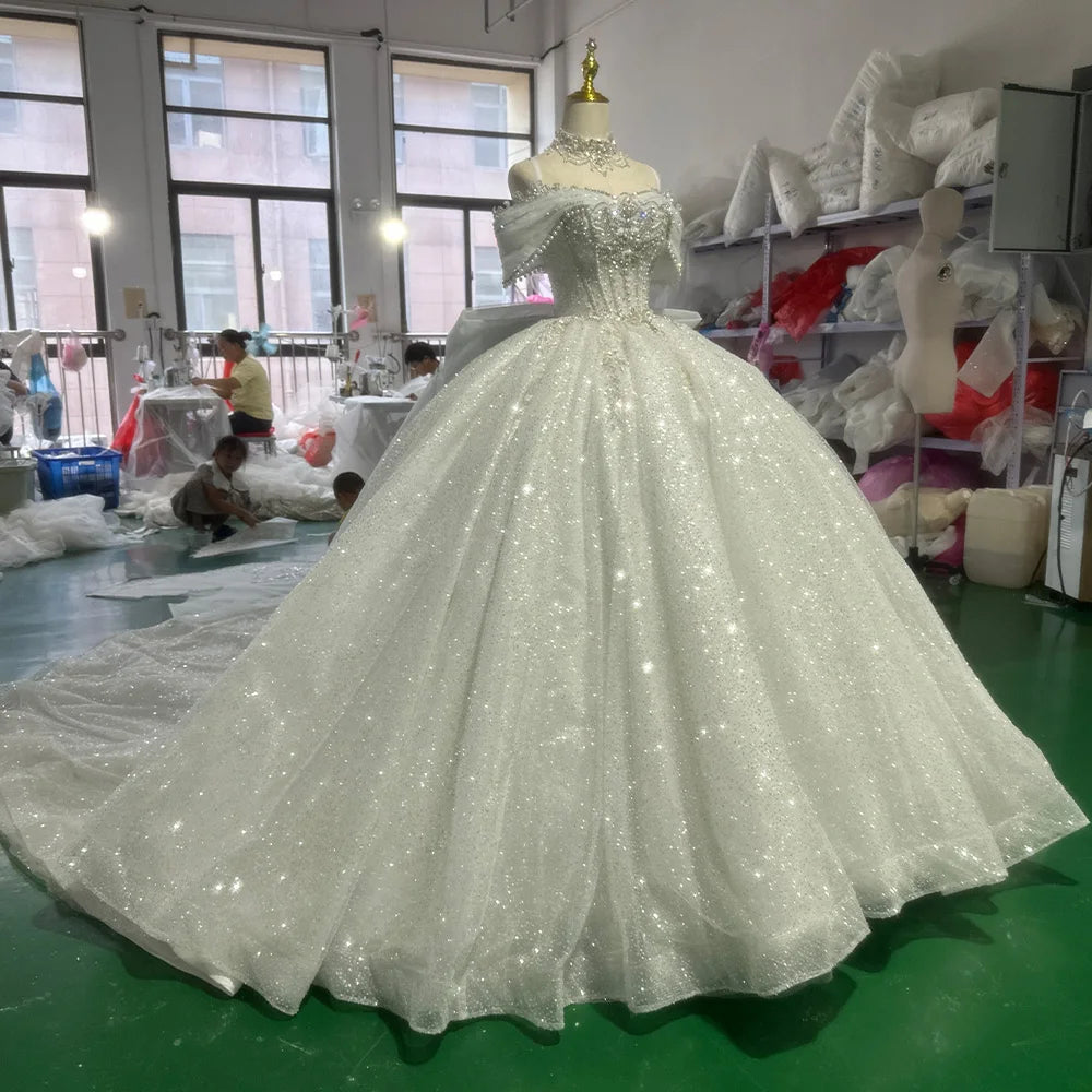 Detailed front view of the off-shoulder bridal gown, emphasizing the intricate beadwork along the waistline and the dramatic spread of the shimmering tulle train.