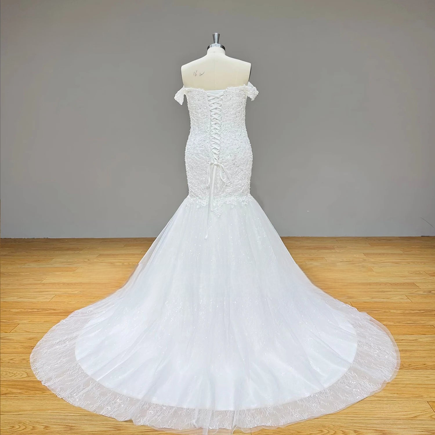 Full-length back view of a tulle mermaid wedding gown on a mannequin, showcasing the structured lace-up corset closure and a gracefully sweeping train.