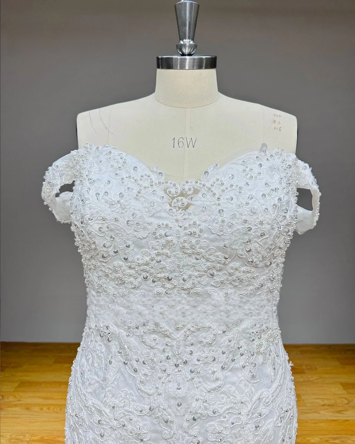 Front close-up of a sweetheart neckline bridal bodice highlighting heavy white pearl clusters, silver beadwork, and intricate scalloped lace appliques.